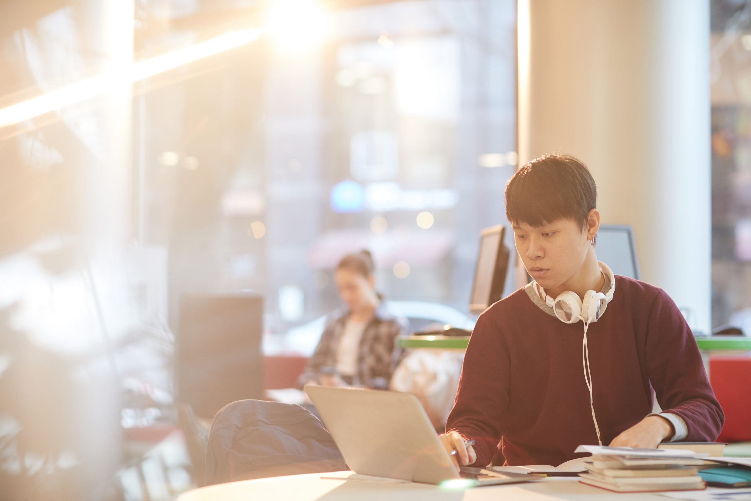 Asian college student using laptop computer while sitting at the table in the library