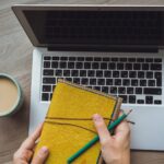 Laptop and coffee cup in girl's hands sitting on a wooden background by Boyarkinamarina