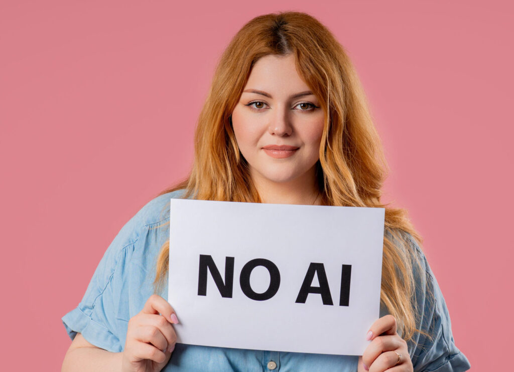 A woman standing on pink wall, holding handmade sign NO AI. Sad confident expression.
